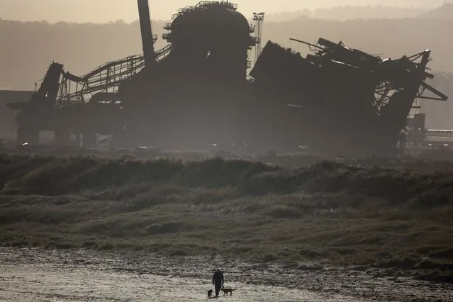 A man walks his dogs in front of the partially demolished blast furnace at the former British Steel plant near Redcar, Britain on January 30, 2023. (Photo by Phil Noble/Reuters)
