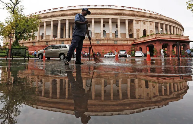 Indian parliament building is reflected in a puddle after the rain as a man sweeps the water in New Delhi, India July 20, 2018. (Photo by Adnan Abidi/Reuters)