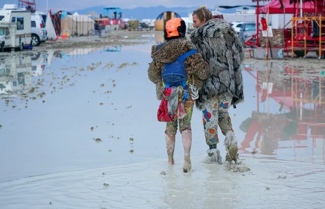Dub Kitty and Ben Joos, of Idaho and Nevada, walk through the mud at Burning Man after a night of dancing with friends in Black Rock City, in the Nevada desert, after a rainstorm turned the site into mud on September 2, 2023. (Photo by Trevor Hughes/USA Today Network via Reuters)