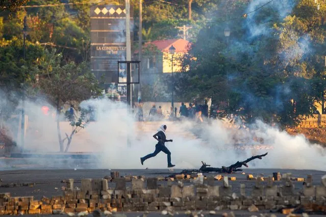 A demonstrator runs during clashes with police amid protests to demand the resignation of President Jovenel Moise in Port-au-Prince, Haiti, 28 February 2021. The opposition demands that the President leave power immediately to allow a transition of power. (Photo by Jean Marc Herve Abelard/EPA/EFE)