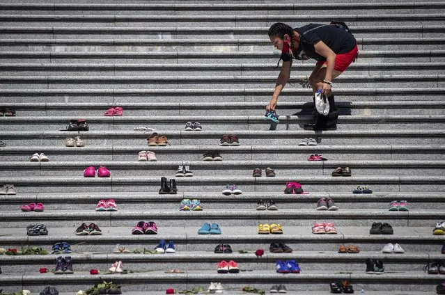 Lorelei Williams places one of 215 pairs of children's shoes on the steps of the Vancouver Art Gallery as a memorial to the 215 children whose remains have been found buried at the site of a former residential school in Kamloops, in Vancouver, British Columbia, Canada on Friday, May 28, 2021. Chief Rosanne Casimir of the Tk'emlups te Secwepemc First Nation said in a news release Thursday that the remains were confirmed last weekend with the help of a ground-penetrating radar specialist. (Photo by Darryl Dyck/The Canadian Press via AP Photo)