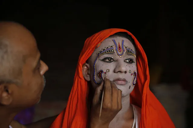 An Indian man applies make up on an artist dressing up as Hindu god Rama ahead of a religious procession during the Dussehra festival in Allahabad, India, Tuesday, October 16, 2018. The Hindu festival of Dussehra commemorates the triumph of Lord Rama over the demon king Ravana, marking the victory of good over evil. (Photo by Rajesh Kumar Singh/AP Photo)