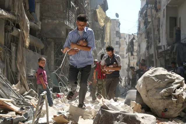 Syrian men carrying babies make their way through the rubble of destroyed buildings following a reported air strike on the rebel-held Salihin neighbourhood of the northern city of Aleppo, on September 11, 2016. Air strikes have killed dozens in rebel-held parts of Syria as the opposition considers whether to join a US-Russia truce deal due to take effect on September 12. (Photo by Ameer Alhalbi/AFP Photo)