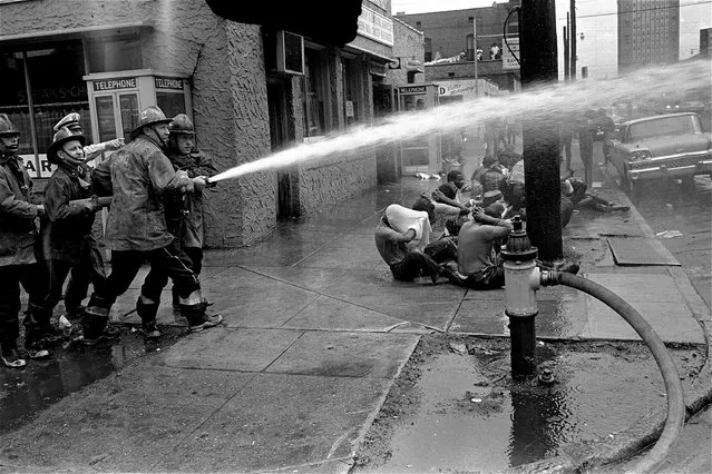 Firemen ignore seated demonstrators on a Birmingham, Ala. sidewalk, May 3, 1963, and turn their water hoses across the street to disperse a jeering crowd of blacks. (Photo by AP Photo)