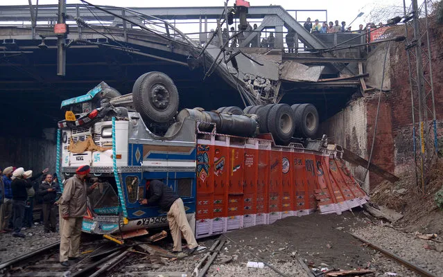 Indian Punjab police personnel inspect an upturned truck, overloaded with sand, which landed on the railway tracks when the oldest bridge on which it was travelling collapsed, in Amritsar on December 6, 2013. No injury or casualty was reported and all trains were delayed for three hours due to this mishap. (Photo by Narinder Nanu/AFP Photo)