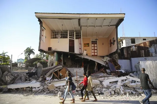 People walk past a home destroyed by the earthquake in Les Cayes, Haiti, Saturday, August 14, 2021. (Photo by Joseph Odelyn/AP Photo)
