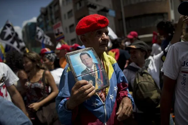 In this Saturday, March 16, 2019 photo, a supporter of Venezuela's President Nicolas Maduro holds a picture of the late President Hugo Chavez during an anti-imperialist march in Caracas, Venezuela. Many were clad in red, the color associated with the movement led by Chavez, the former military officer who declared a socialist “revolution” after coming to power in 1999. (Photo by Ariana Cubillos/AP Photo)