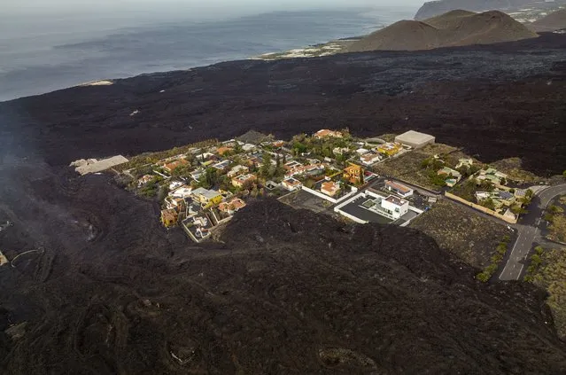 Houses remain isolated as lava from a volcano flows on the Canary island of La Palma, Spain, Monday, December 6 2021. (Photo by Emilio Morenatti/AP Photo)