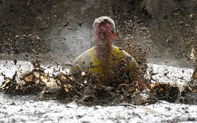 A runner jumps in a mud pit as he takes part in the Mud Day, a 13km race with obstacles in Beynes, near Paris on June 16, 2019. (Photo by Alain Jocard/AFP Photo)