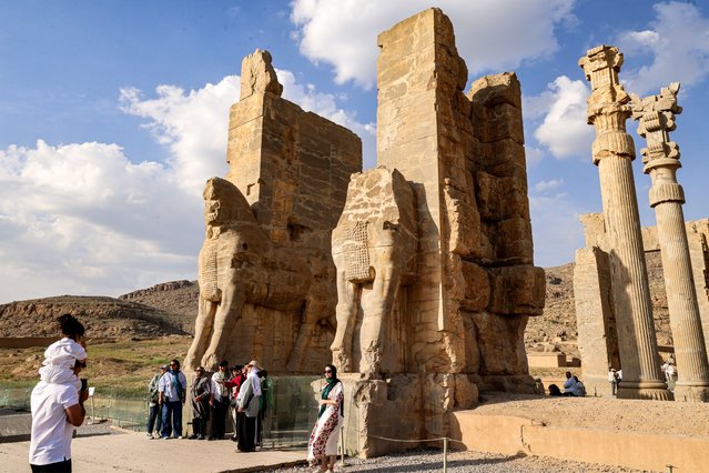 A woman poses for a picture before an ancient gate while touring through the ruins of ancient Persepolis, which served as the capital of the Achaemenid Persian Empire (550-330 BC), in southern Iran on May 13, 2024. (Photo by Atta Kenare/AFP Photo)