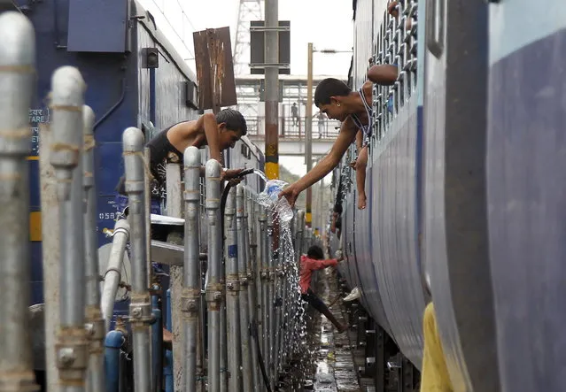 A passenger (R) fills water in a bottle from a pipe that supplies water to trains at a railway station on a hot summer day in Allahabad, June 11, 2015. (Photo by Jitendra Prakash/Reuters)