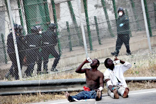 Sub-Saharan migrants drink water as they sit on Spanish soil after jumping a metallic fence that divides Morocco and the Spanish enclave of Melilla, Thursday, May 1, 2014. Spain says around 700 African migrants have rushed its barbed wire border fences in the North African enclave of Melilla, and although police repelled most, 140 managed to enter Spanish territory. The migrants charged the fences in two waves, with 500 arriving in the early hours and another 200 later Thursday morning. (Photo by Fernando Garcia/AP Photo)