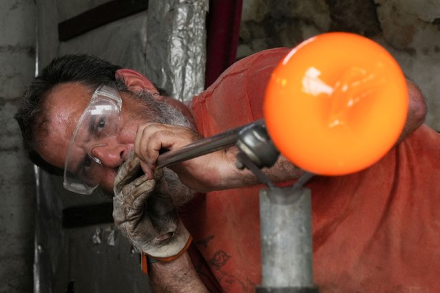 Glassmaker Eduardo Viciana blows molten glass in his atelier in Havana, Cuba, on June 21, 2024. (Photo by Alexandre Meneghini/Reuters)