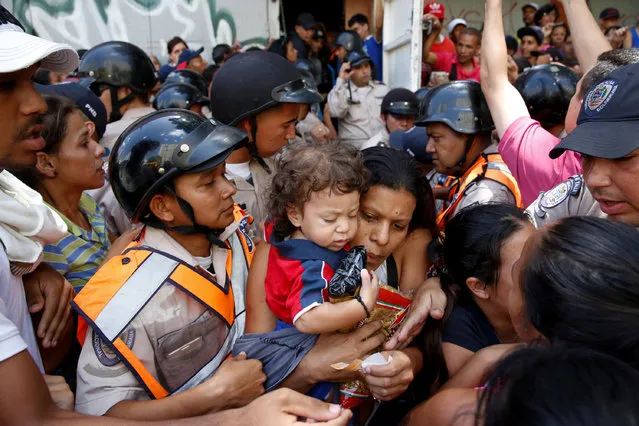 A woman carrying a child and packages of pasta tries to walk out from a gathering outside a supermarket in Caracas, Venezuela, June 10, 2016. (Photo by Carlos Garcia Rawlins/Reuters)