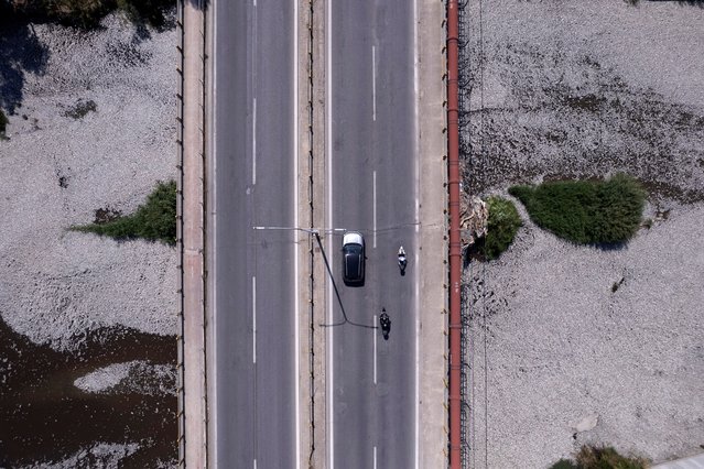 A drone view shows vehicles passing a bridge over a stream with hundreds of thousands of dead fish, near the port of Volos, Greece on August 30, 2024. (Photo by Giannis Floulis/Reuters)