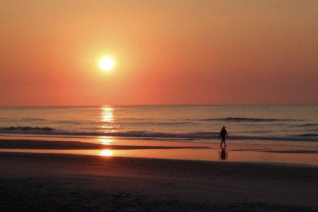 A woman walks down the beach as the sun rises on Wrightsville, Beach, N.C., Tuesday, May 16, 2017. (Photo by Chuck Burton/AP Photo)