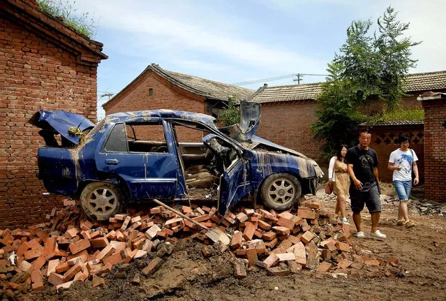 People walk past a flood damaged vehicle in Beijing on July 23, 2012. China's flood-ravaged capital experienced the heaviest rain in six decades killing 37 people. (Photo by Andy Wong/Associated Press)