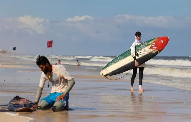 Sabah Abu Ghanem, a 22-year-old Palestinian surfer, carries her surf board before training with her brother, off the shore of Gaza City, on June 13, 2022. (Photo by Mohammed Abed/AFP Photo)