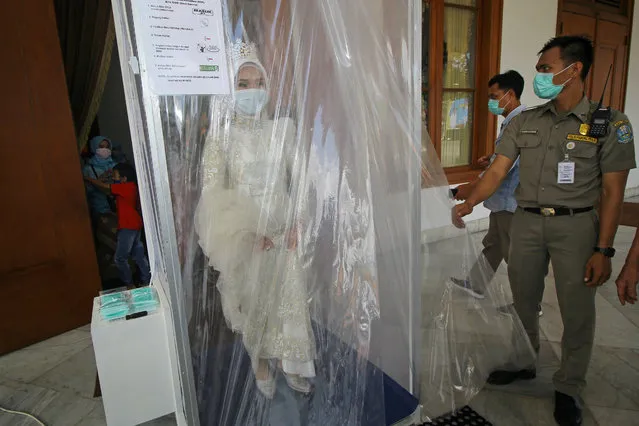 An Indonesian bride wearing a face mask is sprayed inside a disinfection chamber on her wedding day, amid the coronavirus disease (COVID-19) outbreak in Surabaya, East Java Province, Indonesia on March 25, 2020. (Photo by Moch Asim/Antara Foto via Reuters)