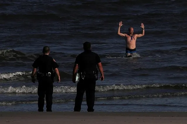 Surrounded by police, a man exits a closed beach with his arms raised during the coronavirus disease (COVID -19) pandemic in Galveston, Texas, U.S., April 26, 2020. Police gave chase after the man repeatedly walked onto nearby Seawall Boulevard, disrupting vehicle traffic, bystanders said. (Photo by Adrees Latif/Reuters)