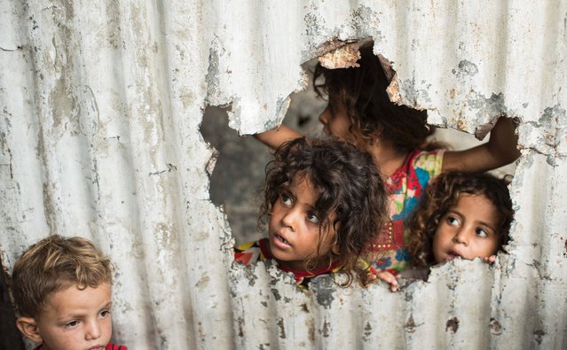Palestinian children look through a hole in a sheet metal fence outside their home in a poor neighbourhood in Gaza City on August 8, 2017. (Photo by Mahmud Hams/AFP Photo)