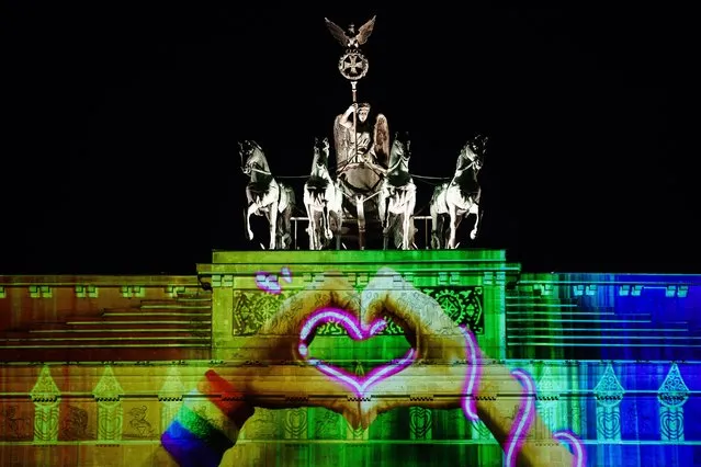 Hands forming a heart with a rainbow colored sweatband are projected on the Brandenburg Gate during the Festival of Lights in Berlin, Germany, 07 October 2022. During the festival, buildings and landmarks of the German capital are screened with light installations and 3D projections. The festival takes place from 07 to 16 October 2022 in 35 places showing 70 installations. (Photo by Clemens Bilan/EPA/EFE)