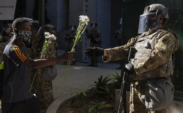 A demonstrator offers flowers to a National Guardsman stationed outside the office of Los Angeles County District Attorney Jackie Lacey, Wednesday, June 3, 2020, in Los Angeles, during a protest over the death of George Floyd, who died May 25 after being restrained by police in Minneapolis. (Photo by Damian Dovarganes/AP Photo)