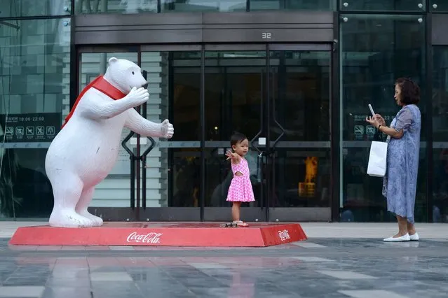 A woman uses her mobile phone to take photos of a girl posing in front of a polar bear model outside a mall in Beijing on August 24, 2016. (Photo by Wang Zhao/AFP Photo)