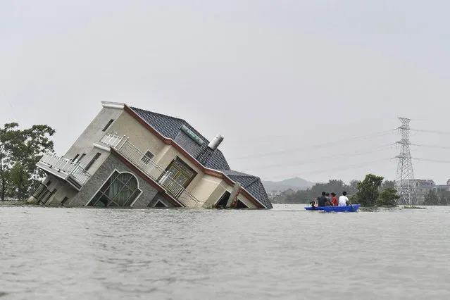 This photo taken on July 15, 2020 shows residents riding a boat past a damaged and flood-affected house near the Poyang Lake due to torrential rains in Poyang county, Shangrao city in China's central Jiangxi province. The vast Yangtze drainage area has been lashed by torrential rains since last month, leaving 141 people dead or missing and forcing the evacuation of millions more across several provinces. (Photo by AFP Photo/China Stringer Network)