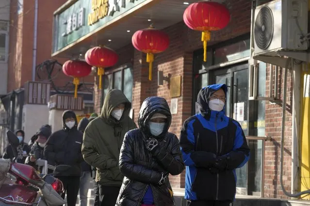 Residents wearing masks line up during a cold day outside a pharmacy to purchase medicine in preparation for a possible wave of COVID-19 outbreaks in Beijing, Tuesday, December 13, 2022. Some Chinese universities say they will allow students to finish the semester from home in hopes of reducing the potential of a bigger COVID-19 outbreak during the January Lunar New Year travel rush. (Photo by Ng Han Guan/AP Photo)