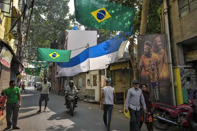 People walk through a street decorated with Brazil's Neymar along with flags of Argentina and Brazil to mark the ongoing soccer World Cup in Kolkata, India, Thursday, December 8, 2022. (Photo by Bikas Das/AP Photo)