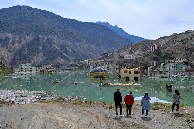 Local residents look on at their town, Yusufeli, submerged by an artificial lake caused by a dam retaining the flow of the Coruh river (also referred to as Chorokhi), Artvin province, in northeastern Turkey, on April 4, 2022. The Yusufeli Dam and its Hydroelectric Power Plant Project in the Eastern Black Sea Region has started to hold water, with the electricity production expected to start in May 2023. With a total water storage volume of approximately 2.2 billion cubic meters, the double curvature concrete arch dam is Turkey's highest with a height of 275 meters. (Photo by Yasin Akgul/AFP Photo)
