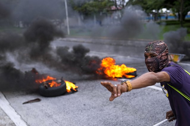 A masked protester shouts to his colleagues as they block a street with burning tires as part of the national strike by the construction union, SUNTRACS, in Panama City, Thursday, June 20, 2024. (Photo by Matias Delacroix/AP Photo)