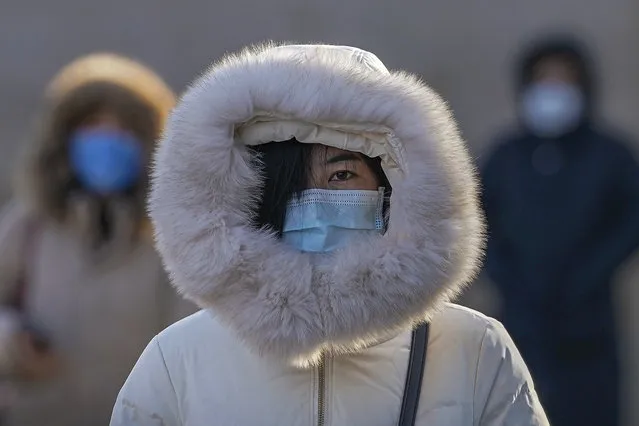 People wearing face masks to help curb the spread of the coronavirus and covered with fur hoods walk on a street as capital city is hit by cold wind in Beijing, Wednesday, January 6, 2021. (Photo by Andy Wong/AP Photo)