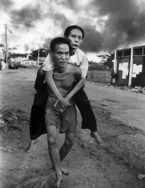 A Vietnamese man carries his lightly wounded wife out of a threatened area in Southern Saigon, Vietnam on May 8, 1968. Daylong fighting in the area erupted at dawn with a daring Viet Cong attack on a police station. As they did during the Tet Offensive, residents abandoned their homes escaping to safer parts of the city. (Photo by Eddie Adams/AP Photo)