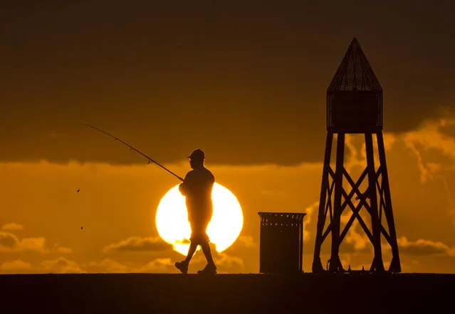 A fisherman prepares to cast a line as the sun rises behind him as he fishes off a jetty into the Atlantic Ocean, Thursday, July 14, 2016, in Bal Harbour, Fla. (Photo by Wilfredo Lee/AP Photo)