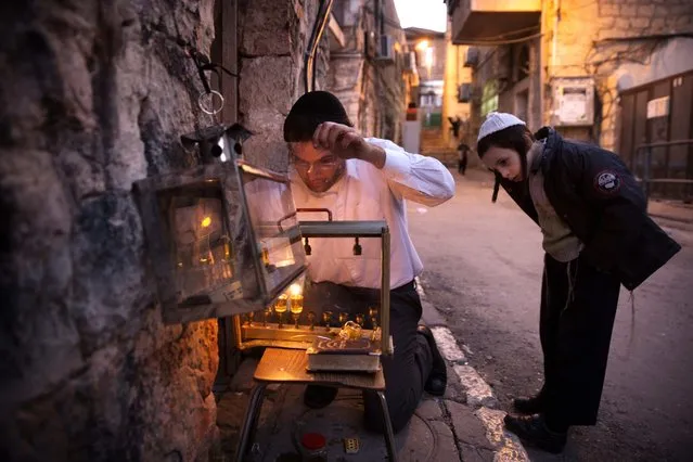 An Ultra-orthodox Jewish man lights candles on the second night of the Jewish holiday of Hanukkah, in a religious neighborhood of Jerusalem, on December 7, 2015. The holiday commemorates the re-dedication of the holy temple in Jerusalem after the Jews' 165 B.C. victory over the Hellenist Syrians when Antiochus, the Greek King of Syria, outlawed Jewish rituals and ordered the Jews to worship Greek gods. (Photo by Menahem Kahana/AFP Photo)