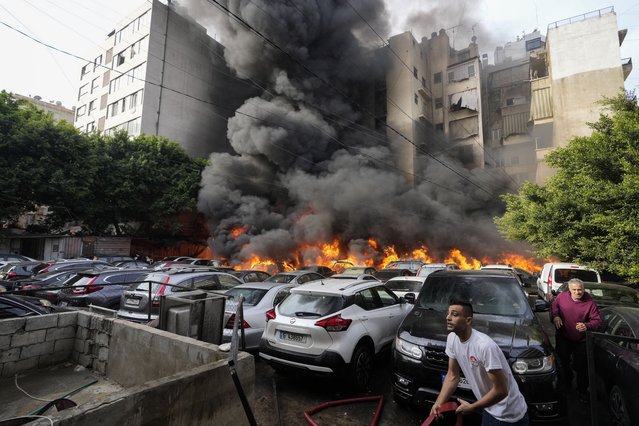 A man runs as a civil defense worker tries to extinguish a fire caused by a giant diesel tank which ignited, burning more than a dozen cars in a parking lot and damaging a building nearby, in a residential Beirut neighborhood, Lebanon, Saturday, November 9, 2024. (Photo by Hassan Ammar/AP Photo)