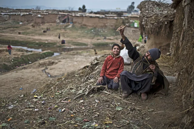 An Afghan refugee man refugee man shows his son how to use a slingshot, in a slum on the outskirts of Islamabad, Pakistan, Wednesday, January 28, 2015. (Photo by Muhammed Muheisen/AP Photo)