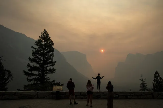 Hannah Whyatt poses for a friend's photo as smoke from the Ferguson fire fills Yosemite Valley, Wednesday, July 25, 2018, in Yosemite National Park, Calif. Campsites and lodges emptied out after disappointed tourists were ordered to leave the heart of Yosemite National Park by noon Wednesday, as firefighters battled to contain a huge wildfire just to the west that has threatened the park's forest and sent up smoke that obscured grand vistas of waterfalls and sheer granite faces. (Photo by Noah Berger/AP Photo)