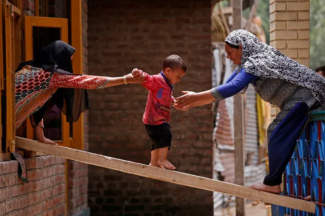 Women help a child to cross over to the other house on a wooden plank after flash floods in Tailbal, on the outskirts of Srinagar July 24, 2018. (Photo by Danish Ismail/Reuters)