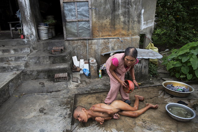Tang Thi Thang baths her disabled son Doan Van Quy outside their family home in Truc Ly, in Vietnam's Quang Binh Province April 11, 2015. Doan Van Quy's father, a soldier who served on 12.7 mm anti-aircraft guns during the Vietnam war, said he lived in several areas that were contaminated by Agent Orange. Two of his sons were born with serious health problems and the family and local health officials link their illnesses to their father's exposure to Agent Orange. (Photo by Damir Sagolj/Reuters)