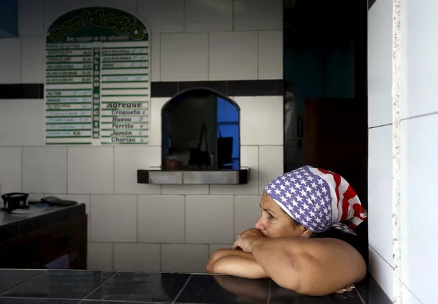 A Cuban woman waits for costumers in her private cafeteria, while wearing a scarf with the colors of the U.S. flag, in Havana April 11, 2015. (Photo by Reuters/Stringer)