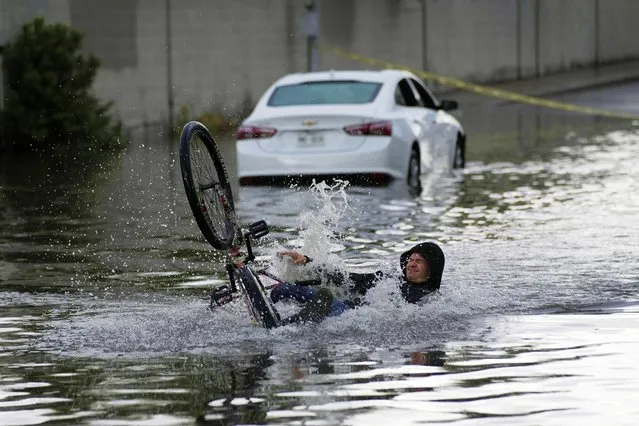 A cyclist falls while trying to ride through floodwaters near a stranded car, Friday, September 1, 2023, in Las Vegas. (Photo by John Locher/AP Photo)