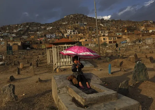 An Afghan girl holds an umbrella as she sits on a grave at a cemetery in Kabul, February 12, 2015. (Photo by Mohammad Ismail/Reuters)