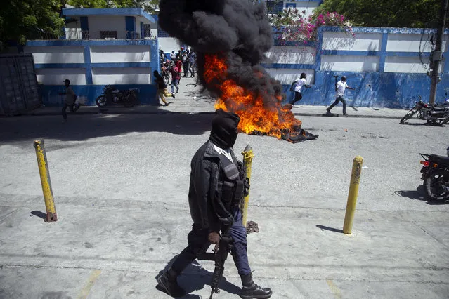 A masked police officer walks with his weapon past a barricade set alight in front of a police station in Delmas, during a protest by a disgruntled sector of the Haitian police force known as Fantom 509, in Port-au-Prince, Haiti, Wednesday, March 17, 2021. The protests started when officers and police academy cadets marched toward police headquarters to demand that the bodies of five officers killed during a raid last week on the Village of God shantytown be recovered from the gang still holding them. Then things escalated when Fantom 509 stormed several police stations in Port-au-Prince, freeing jailed comrades accused of participating in an alleged coup against embattled President Jovenel Moise. (Photo by Dieu Nalio Chery/AP Photo)