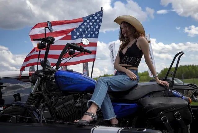 A woman looks on as she sits on a motorcycle next to the U.S. national flag during the Russian Weekend Drags races of U.S. retro and muscle cars, in Bykovo, outside Moscow, Russia on May 16, 2021. (Photo by Maxim Shemetov/Reuters)