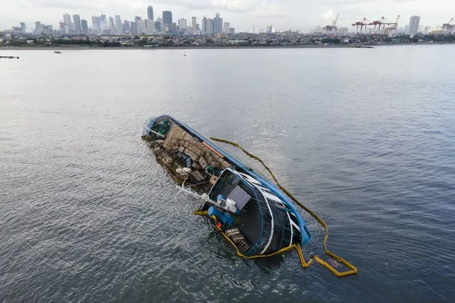 A half-submerged M/V Palawan Pearl is surrounded by an oil spill boom from the Philippine Coast Guard as it lies in the waters of Manila bay, Philippines after it collided with a Cyprus-flagged BKM 104 dredger on Thursday, July 8, 2021. The Philippine cargo vessel and a Cyprus-flagged dredger collided in a Manila Bay anchorage area early Thursday, resulting in no injuries but causing the cargo vessel to list and lie half-submerged in the busy waters. (Photo by Aaron Favila/AP Photo)