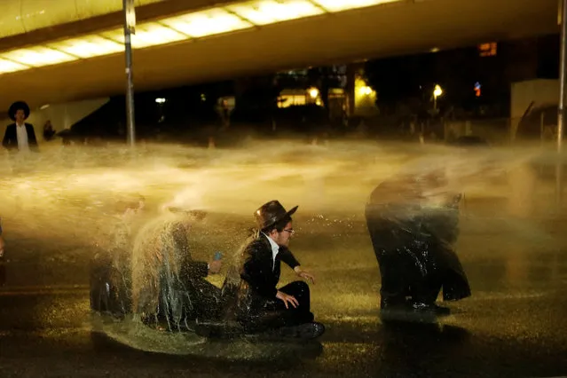 Israeli ultra-Orthodox Jewish men sit as a water cannon is activated during a protest against the detention of a member of their community who refused to serve in the Israeli army, in Jerusalem, March 8, 2018. (Photo by Ronen Zvulun/Reuters)