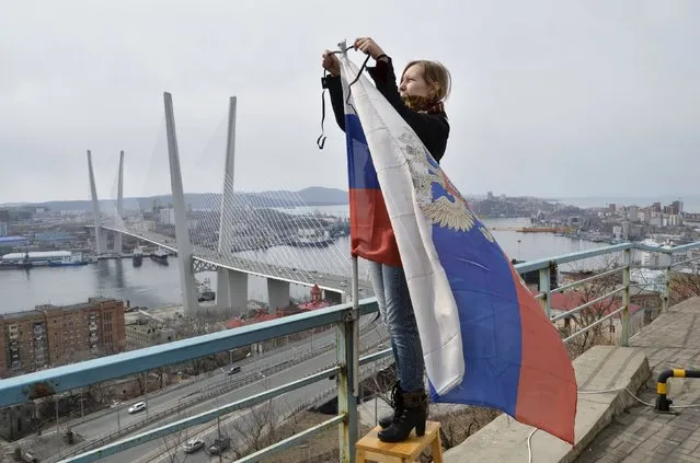 A woman attaches a black ribbon for those killed in the sinking of Dalniy Vostok, to a Russian national flag in Vladivostok April 7, 2015. A Russian trawler Dalniy Vostok sank in the Sea of Okhotsk off Russia's far eastern Kamchatka peninsula on April 2, 2015, killing at least 56 of the 132 crew, the emergencies ministry said on April 2. (Photo by Yuri Maltsev/Reuters)